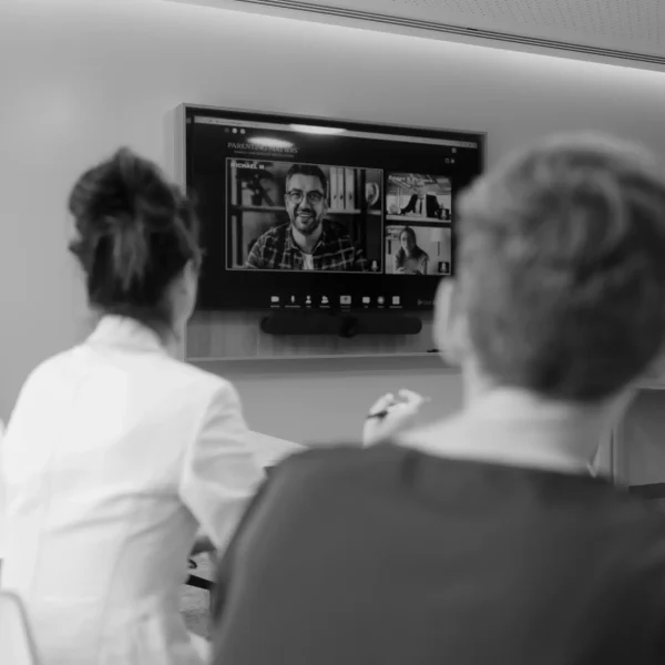 Black and white photo of a video consultation between people displayed on a TV screen